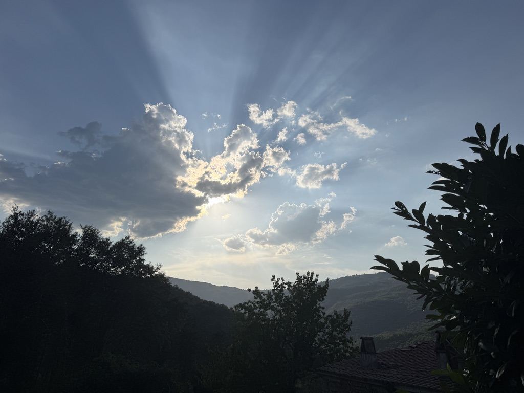 Sun breaking through clouds above the hills at dusk